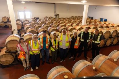 Eight people standing in a room filled with wine barrels