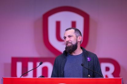 A man speaks at a podium in front of a Unifor sign