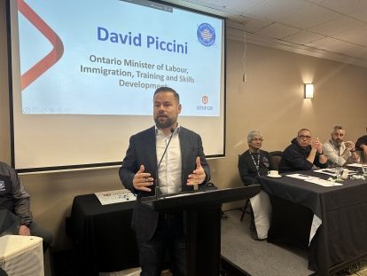 A man speaking in front of a presentation screen.