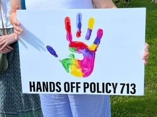 A person holding a sign of a colourful hand print that reads, Hands off policy 713