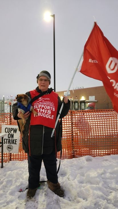 A woman in the snow carrying a red Unifor flag.
