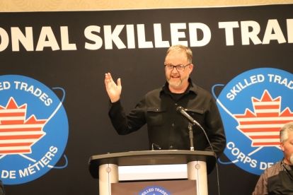 A man with a beard and glasses speaks at a podium