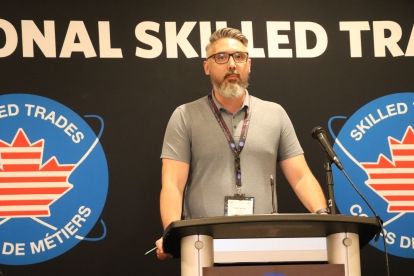 A tall man with a beard and glasses speaking at a podium
