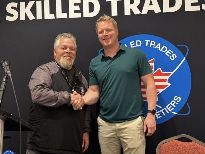 Two man shaking hands in front of a black Unifor Skilled Trades bannner
