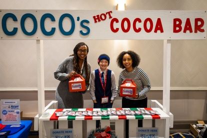 Coco's hot cocoa bar sign, three people at a table holding up packages