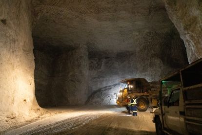 Two people a tractor and truck inside a dark salt mine