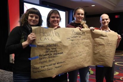four people holding up a large brown paper