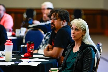 two people sitting at a table looking a head, listing