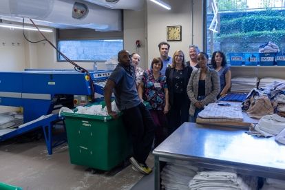 workers in a laundry room posing by steal tables and a large bin