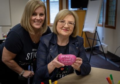 Two women posing one is holing up a coloured rock