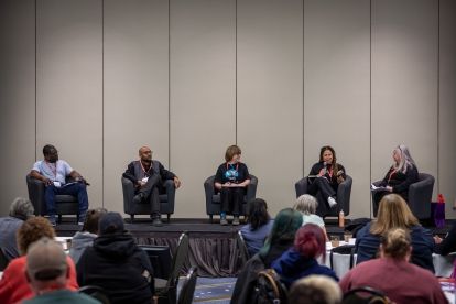 5 people on a stage in arm chairs