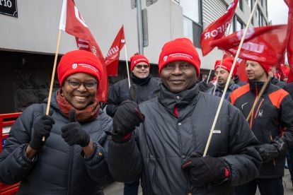 A group of people outside at a rally wearing winter gear red Unifor hats and holding up Unifor flags.