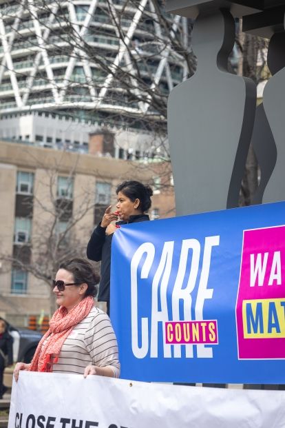 Two women each holding up a banner one is blowing a whistle