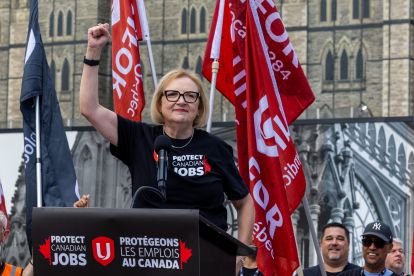 Lana Payne speaks at a podium with Protect Canadian Jobs Unifor logo and red flags behind her.