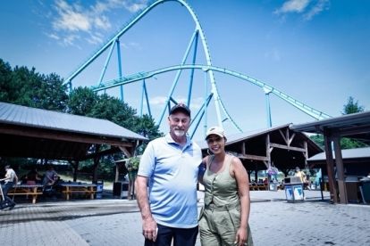 Two people standing in front of a rollercoster