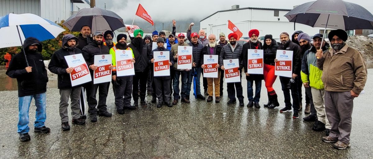 Large group of workers with On Strike signs posing for photo outdoors in wet weather