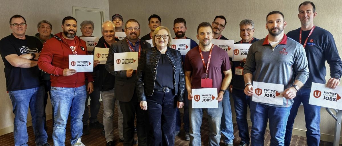 A group of workers standing with Lana Payne holding signs saying "Protect Canadian Jobs".
