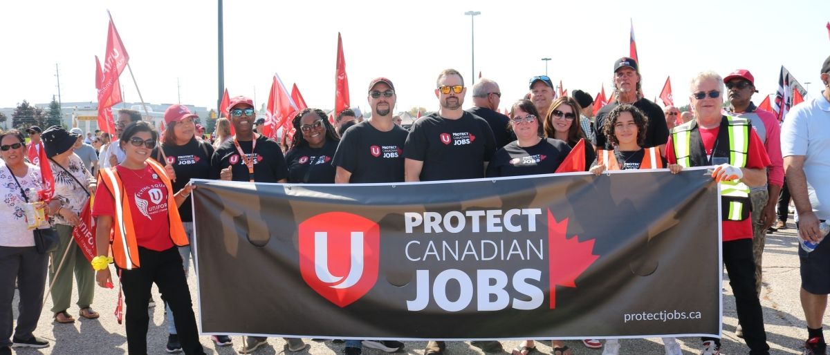 group of people standing outside holding a Protect Canadian Jobs Banner.