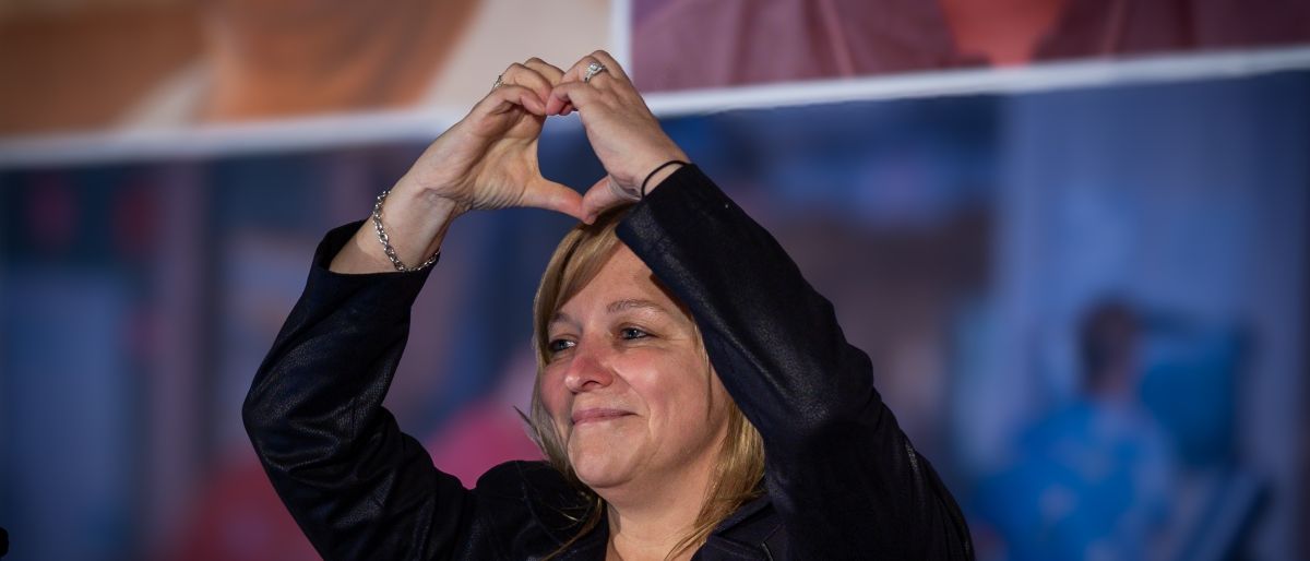 Jenn Murray making a heart shape with her hand overhead 
