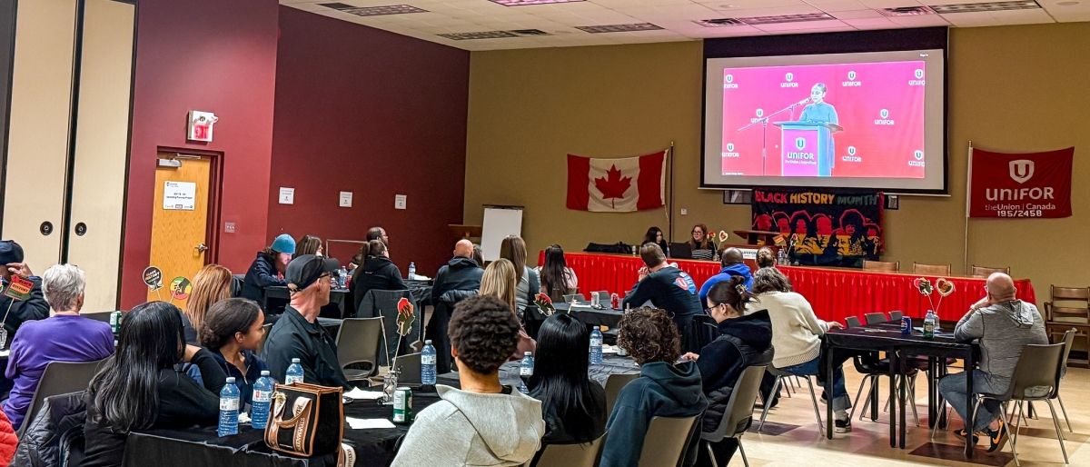People sitting at tables looking forward at a presentation screen.