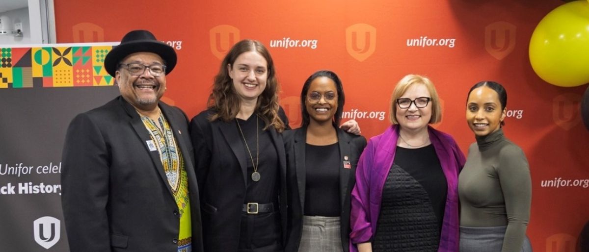 Five people posing in front of a red Unifor backdrop, black history month banner and ballons
