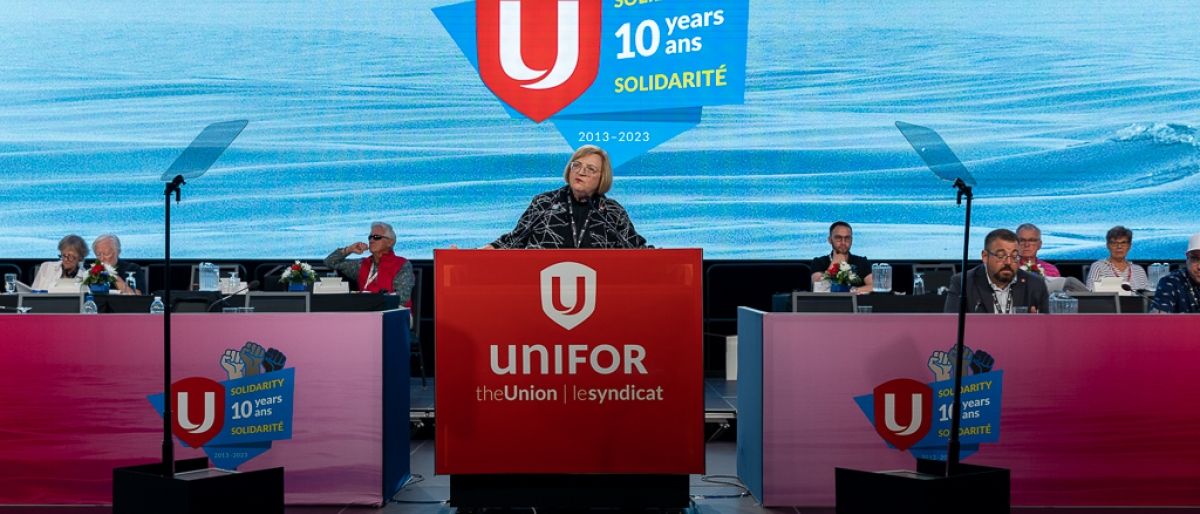 Lana Payne stands at the podium on stage with the Unifor graphic in the background.