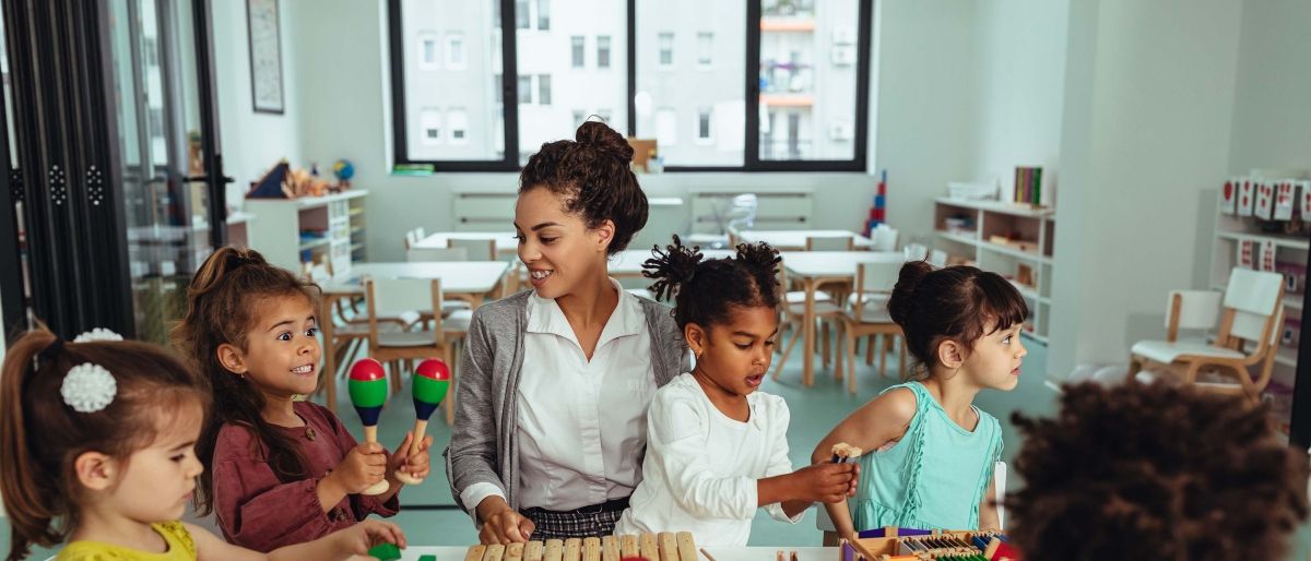 A child care worker sitting at a table with several young children playing games.