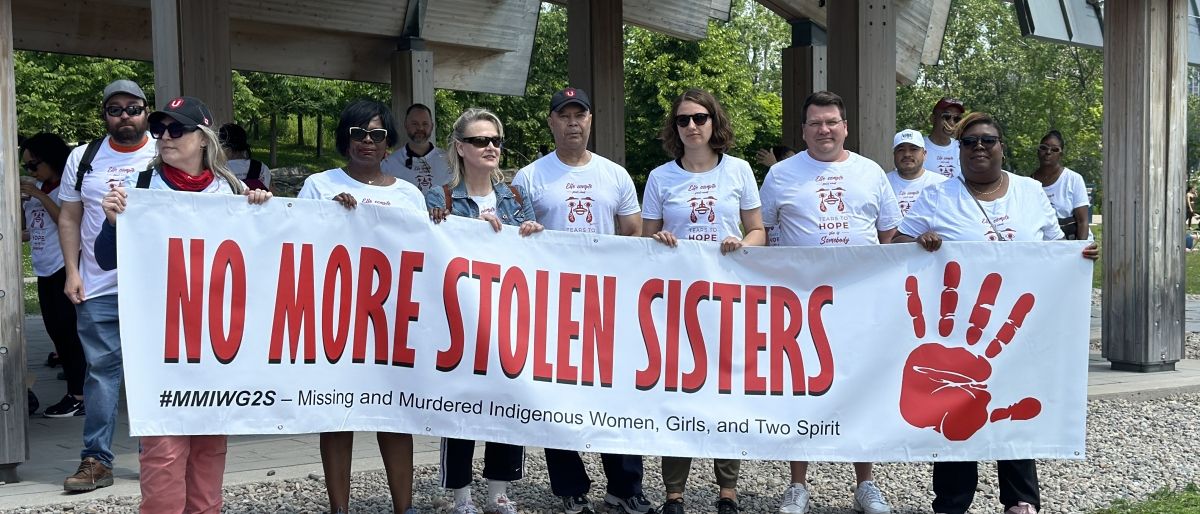 A group of women holding up a large white banner that reads, no more stollen sisters, in red with a red hand print