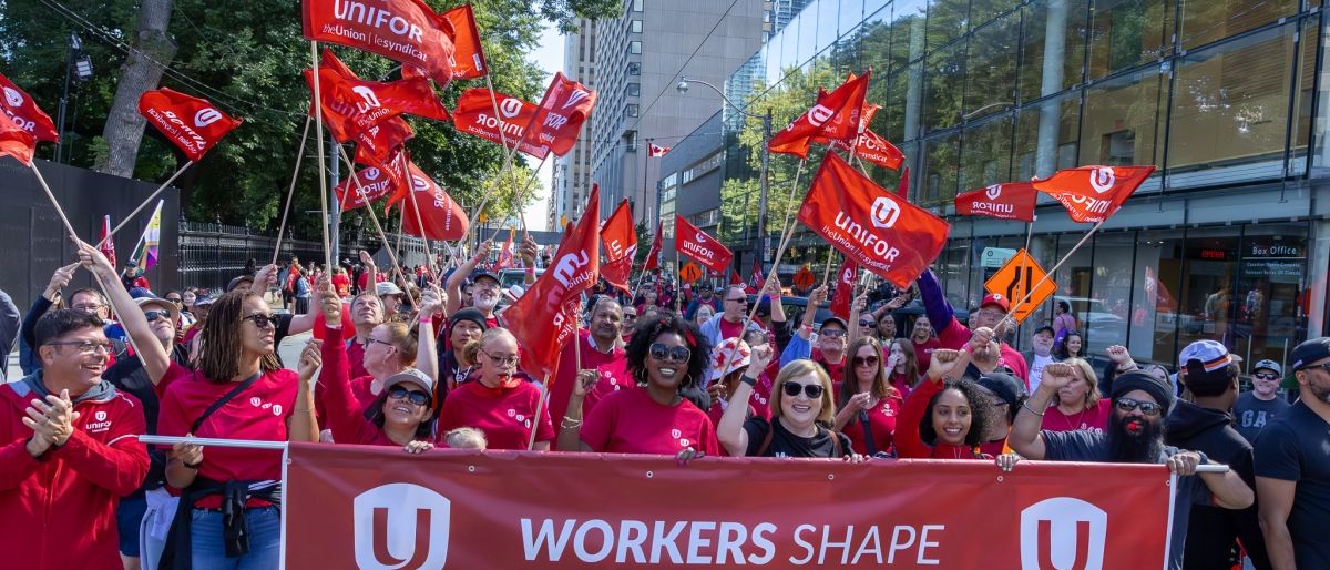 A large group of Unifor members marching behind a banner