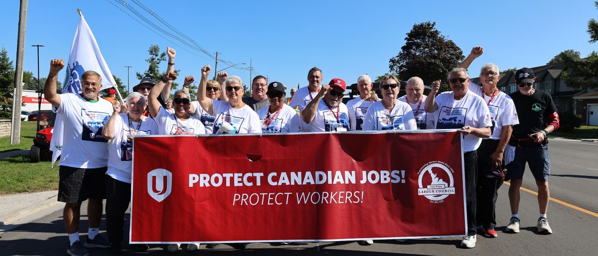 A group of people behing a large red banner "Protect Canadian Jobs" Unifor logo