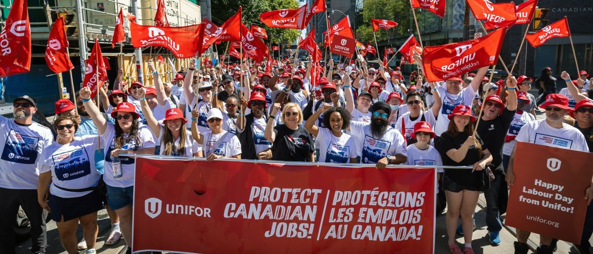 A large crowd behind a red Unifor banner "Protect Canadian Jobs" Unifor logo in white