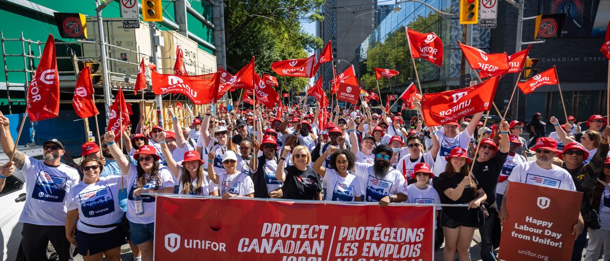 A large crowd behind a red banner "Protect Canadian Jobs" Unifor logo in white