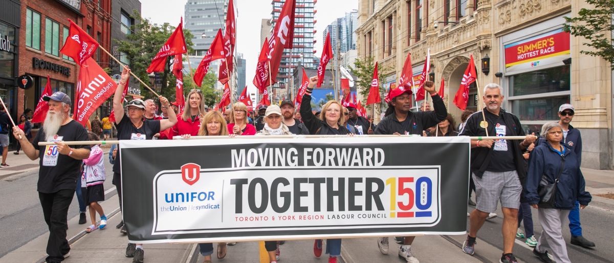 Labour Day 2022 Unifor members at the front of the march holding a parade banner "moving forward together" 150 Toronto and York Region Labour Council