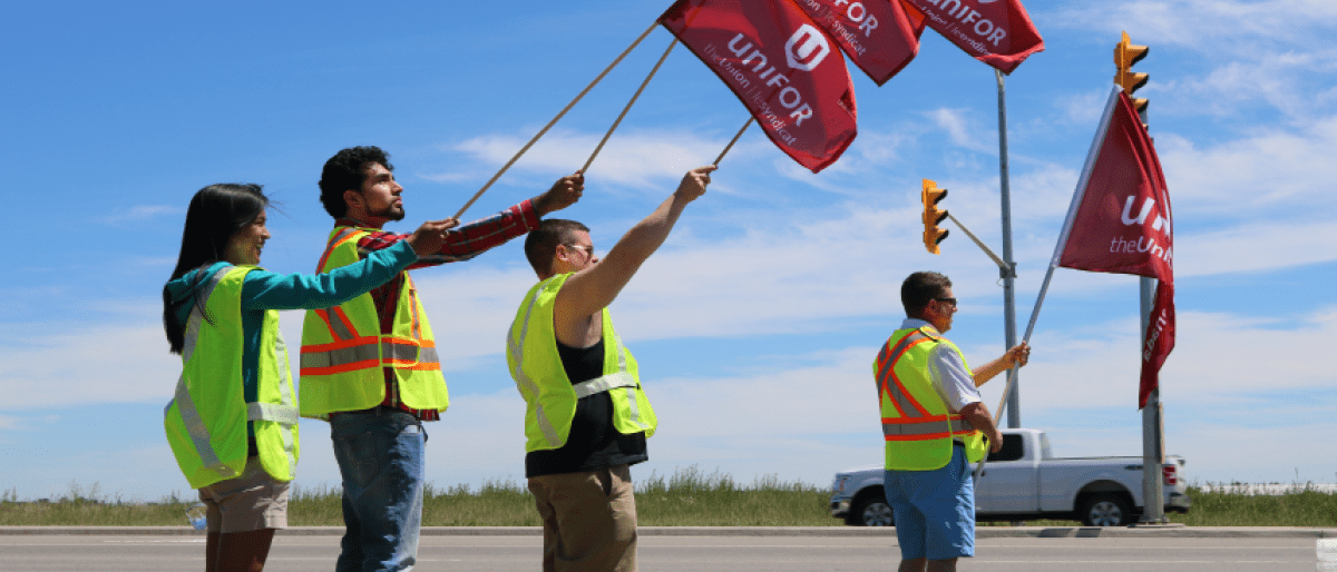 Four Unifor members holding Unifor flags outdoors.