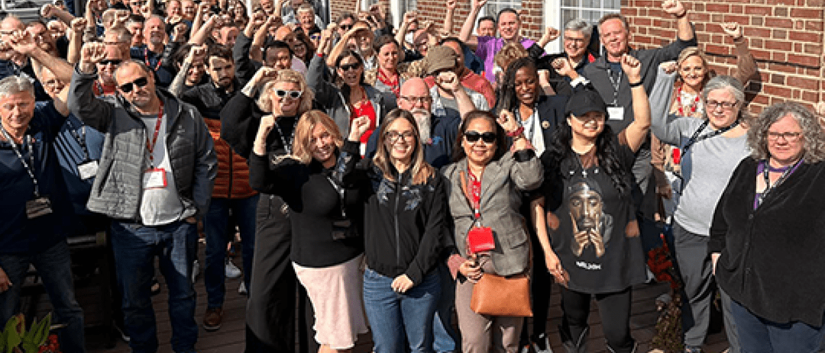 A group of people standing outside a building in the sunshine, fists in the air.