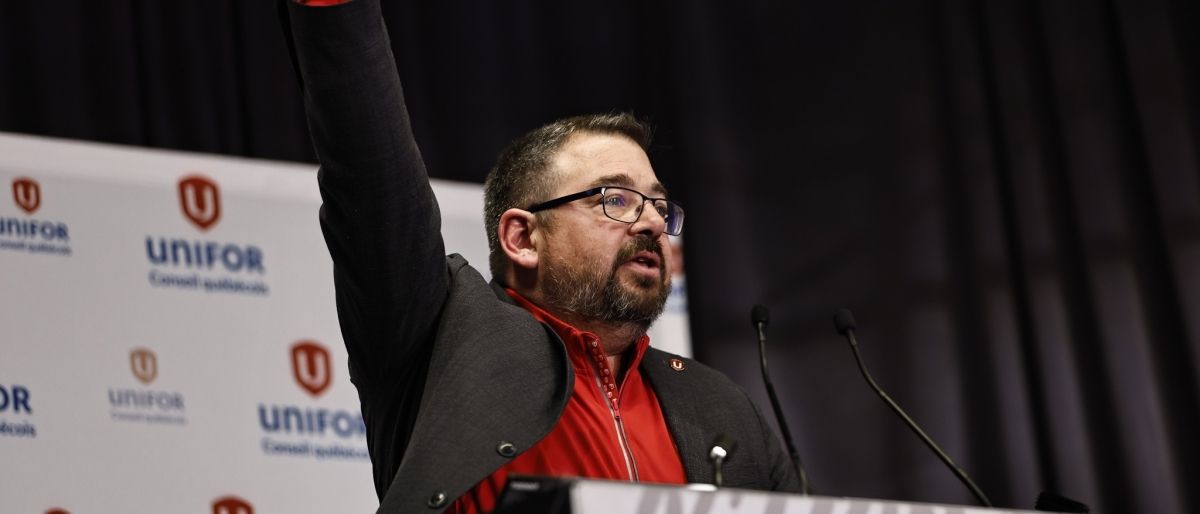Quebec Director Daniel Cloutier at a podium with his fist raised in the air. 