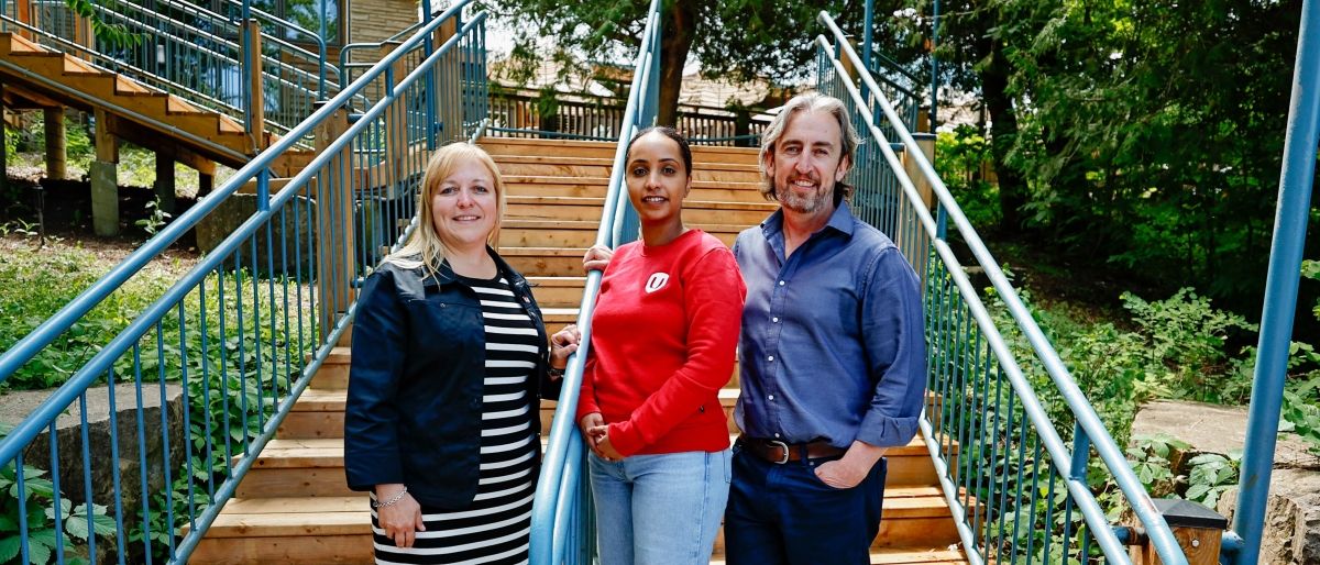 Three people standing at the bottom of a staircase outside