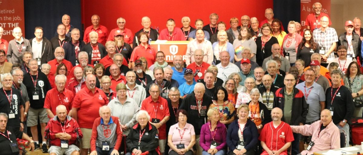 A group of people with a red Unifor stage in the background.