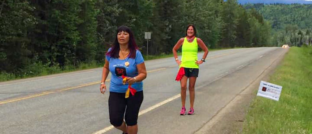 Woman running at the side of a rural highway with a woman walking behind her.