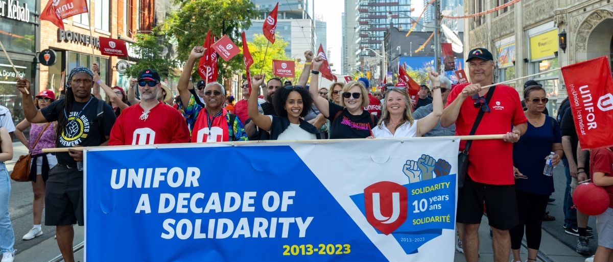 A crowd walking behind a large banner; Unifor a decade of Solidarity