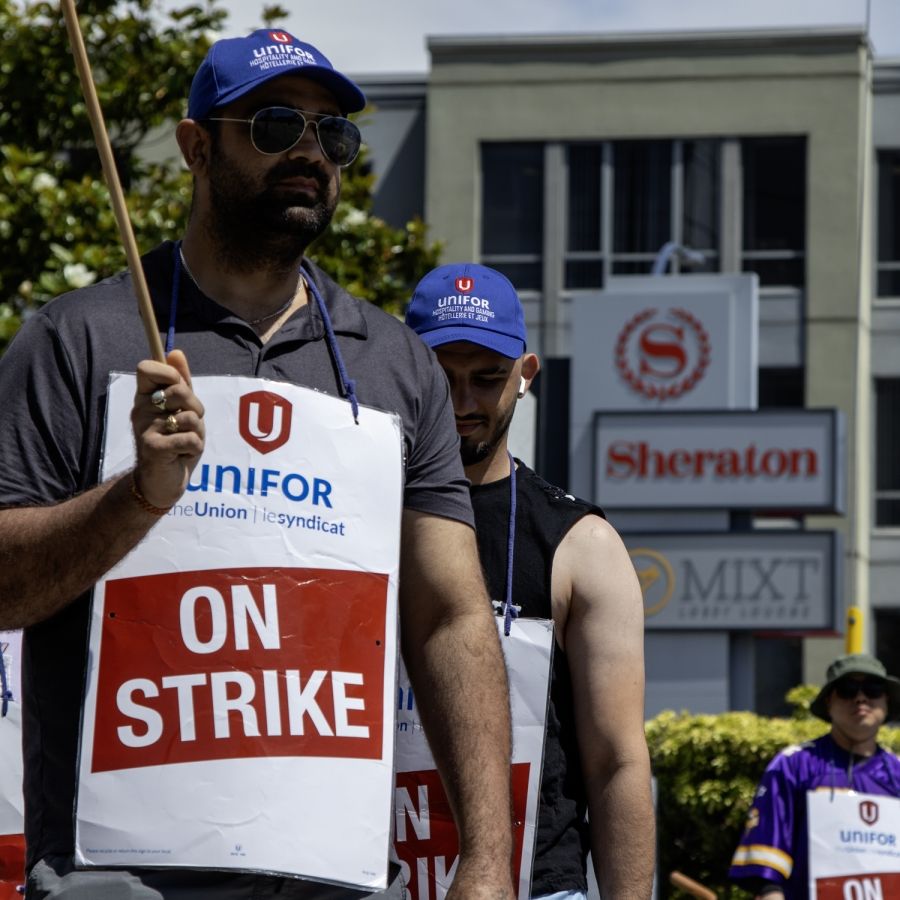 Striking members on a picket line wearing "On Strike" signs