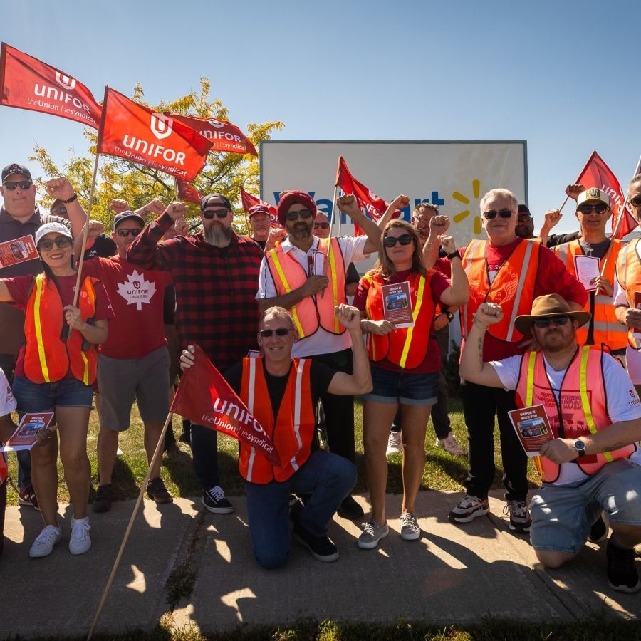 A large group holding Unifor flags wearing safey vests