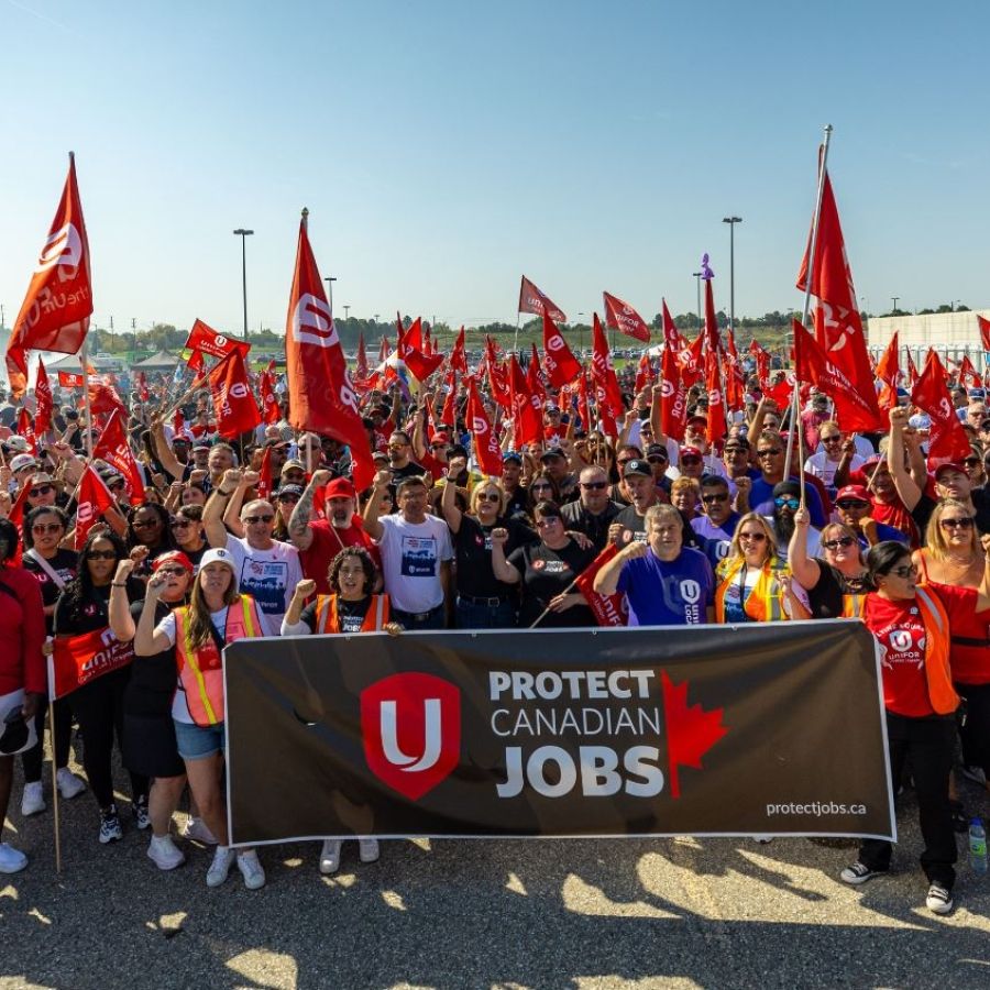 A large group of people at a Unifor rally in Brampton holding Unifor flags