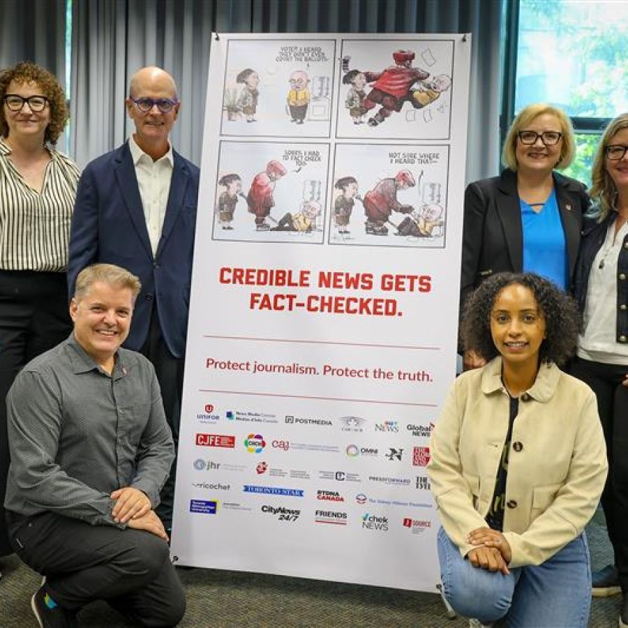 six people beside a x-stand banner, Credible news gets fack checked.