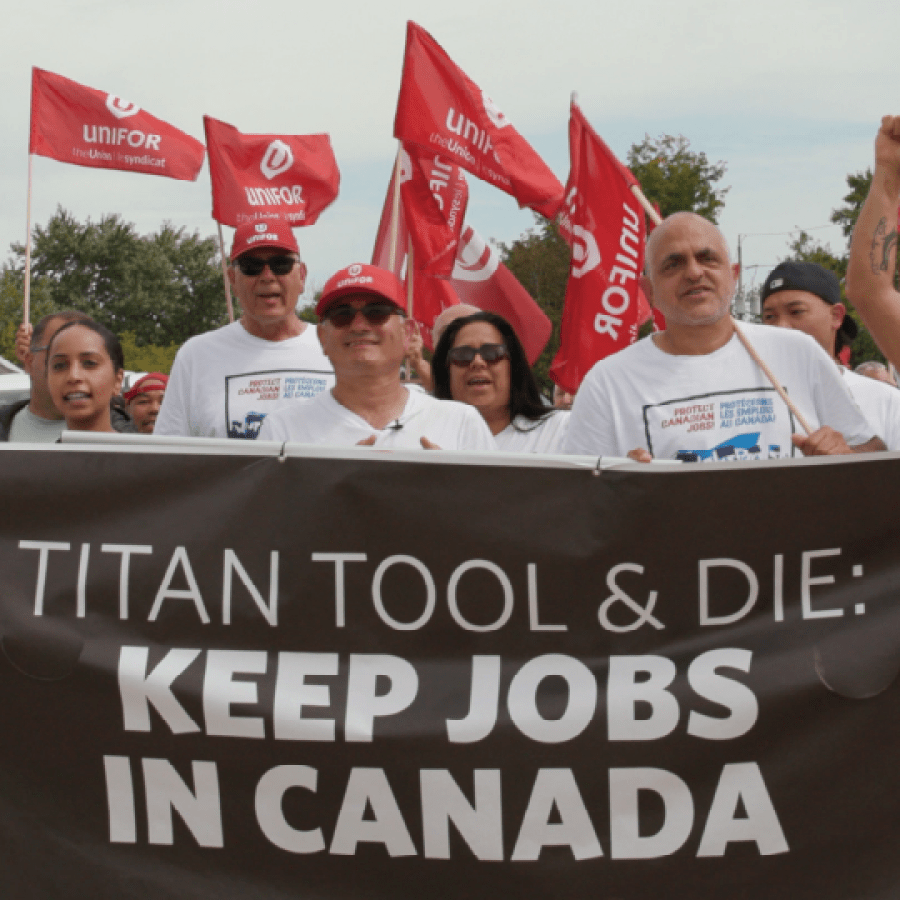 Unifor members and supporters hold a large banner reading “Titan Tool & Die: Keep Jobs in Canada” while raising fists and standing in front of a sea of red Unifor flags at a rally.