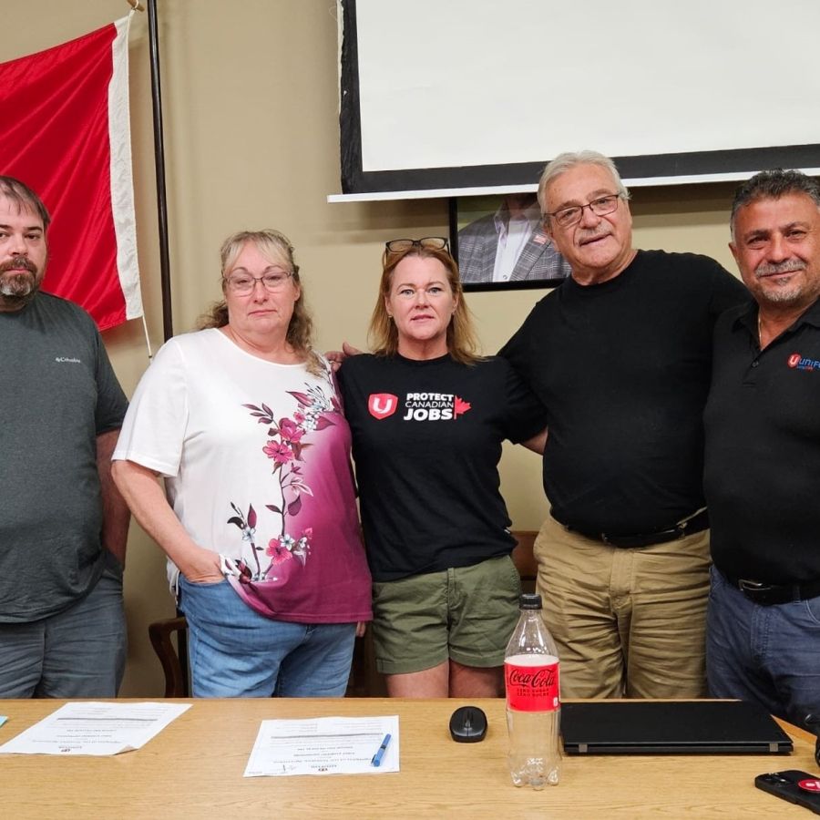 A group of five people standing at a table with papers on them.