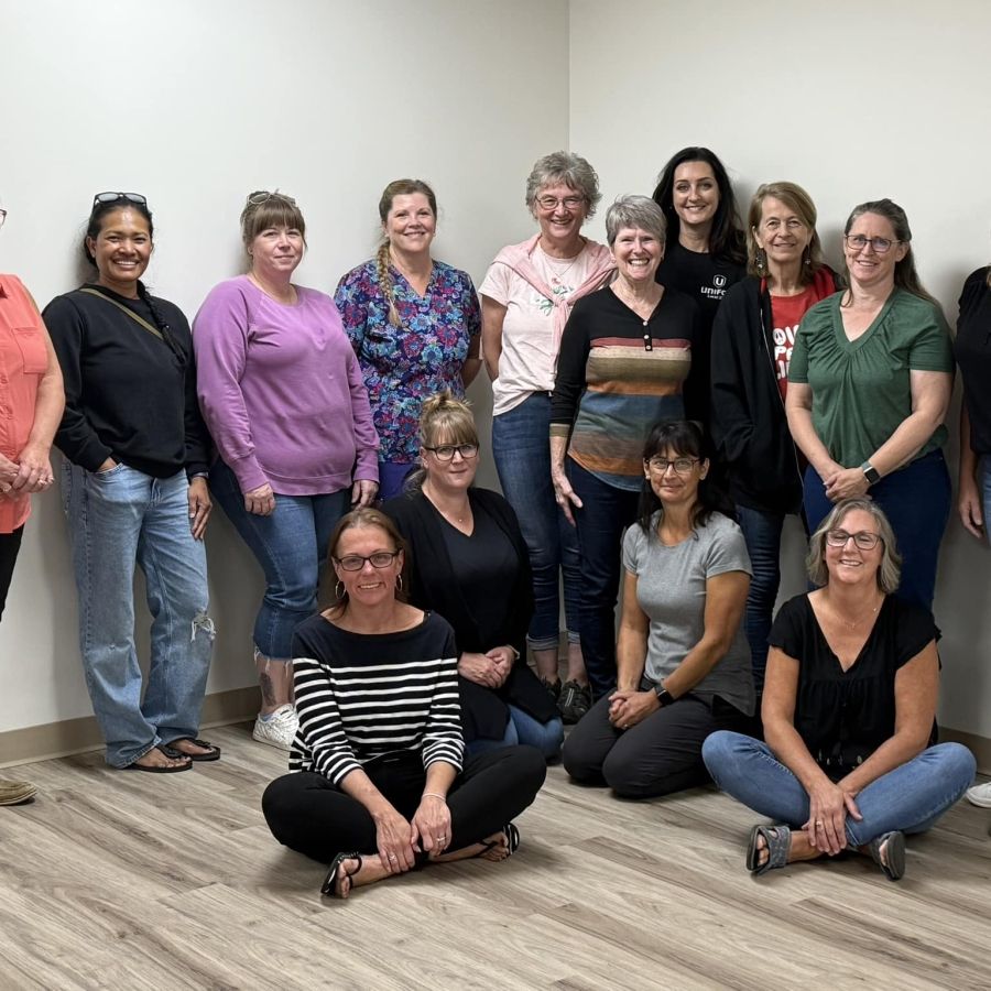A group of women posing four sitting on the floor in front on a wood floor in the corner of the room.